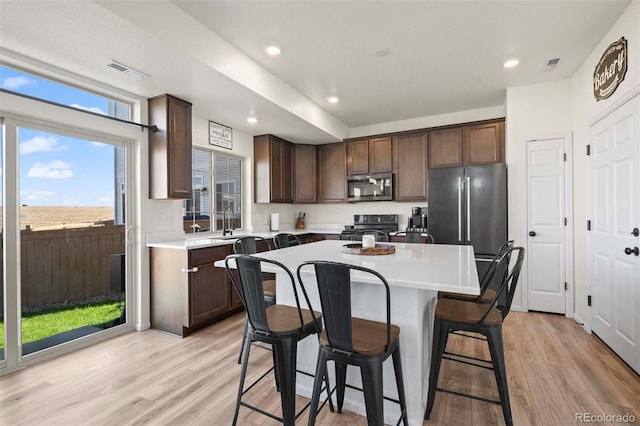 kitchen with a kitchen island, dark brown cabinets, stainless steel appliances, a kitchen breakfast bar, and light hardwood / wood-style floors