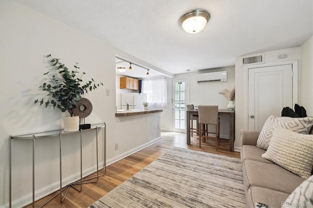 living room with a wall mounted AC, wood finished floors, and baseboards