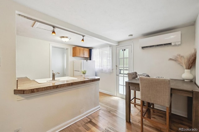 kitchen featuring a wall mounted air conditioner, freestanding refrigerator, light wood-type flooring, a peninsula, and a sink