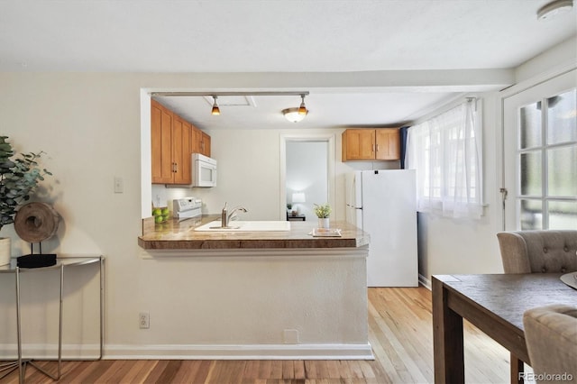 kitchen featuring white appliances, light wood finished floors, a peninsula, brown cabinets, and a sink