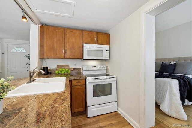 kitchen with white appliances, a sink, tile countertops, brown cabinetry, and light wood-style flooring