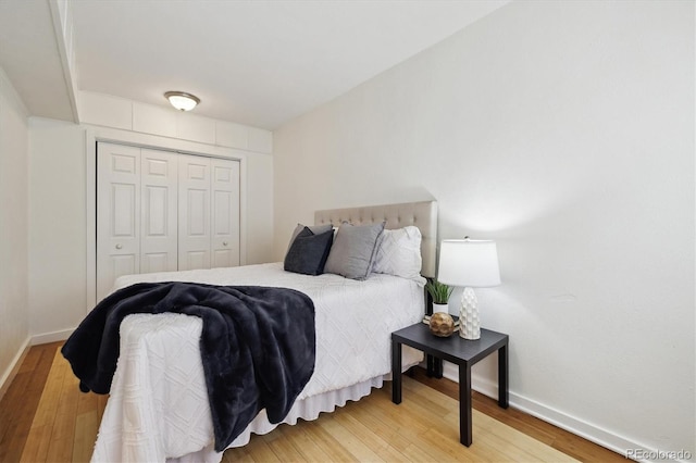 bedroom with light wood-style flooring, baseboards, and a closet