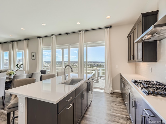 kitchen featuring wall chimney range hood, appliances with stainless steel finishes, a sink, light countertops, and recessed lighting