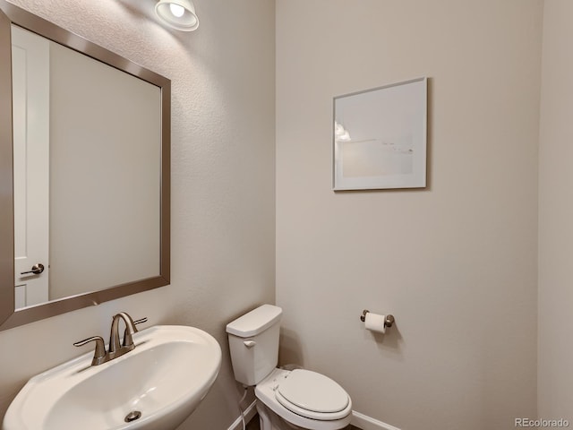 half bath with toilet, baseboards, and a sink