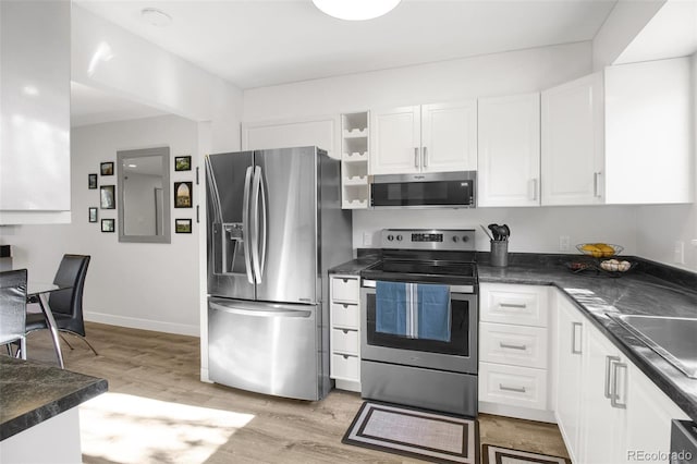 kitchen featuring stainless steel appliances, dark countertops, white cabinetry, and light wood finished floors