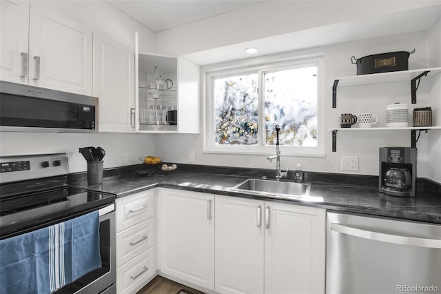 kitchen with appliances with stainless steel finishes, dark countertops, a sink, and white cabinetry