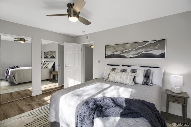 bedroom with multiple closets, visible vents, ceiling fan, wood finished floors, and baseboards