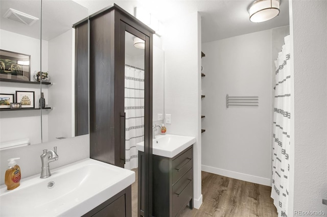 full bath with visible vents, vanity, baseboards, and wood finished floors