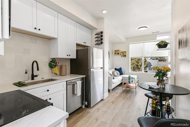 5385 W 14th Ave, Lakewood, CO 80214 - kitchen featuring stainless steel appliances, white cabinetry, light stone countertops, tasteful backsplash, and light wood-type flooring