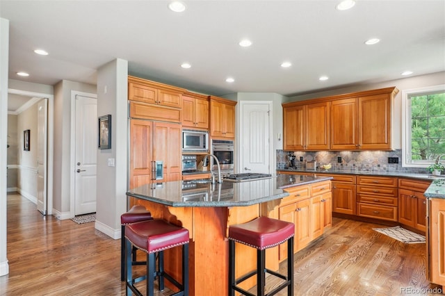 4651 Sonado Pl, Parker, CO 80134 - kitchen featuring built in appliances, a breakfast bar area, light wood-style flooring, decorative backsplash, and a kitchen island with sink