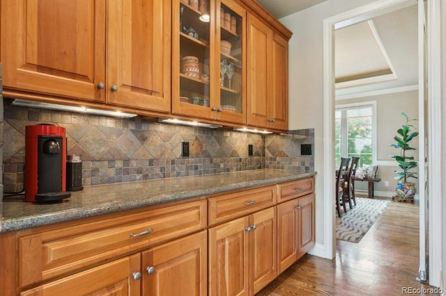 4651 Sonado Pl, Parker, CO 80134 - kitchen featuring crown molding, wood finished floors, glass insert cabinets, brown cabinets, and dark stone countertops