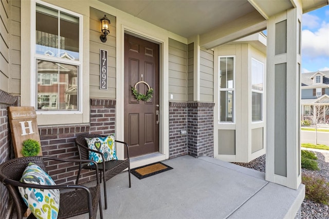 entrance to property featuring a porch and brick siding