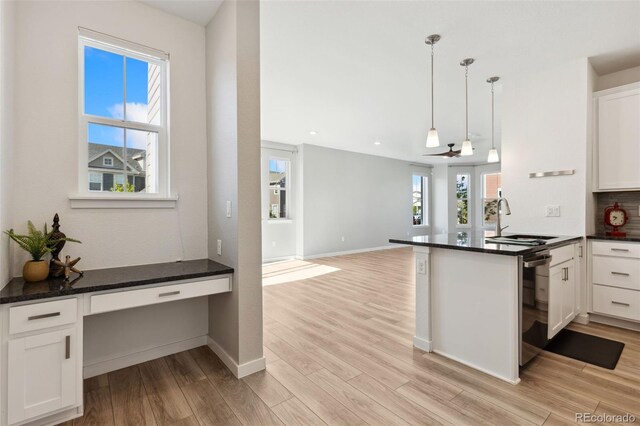 kitchen featuring a sink, light wood-style flooring, white cabinets, dishwashing machine, and a peninsula