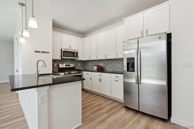 kitchen with appliances with stainless steel finishes, light wood-style floors, tasteful backsplash, white cabinetry, and a sink