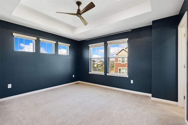 carpeted spare room featuring a tray ceiling, ceiling fan, and baseboards