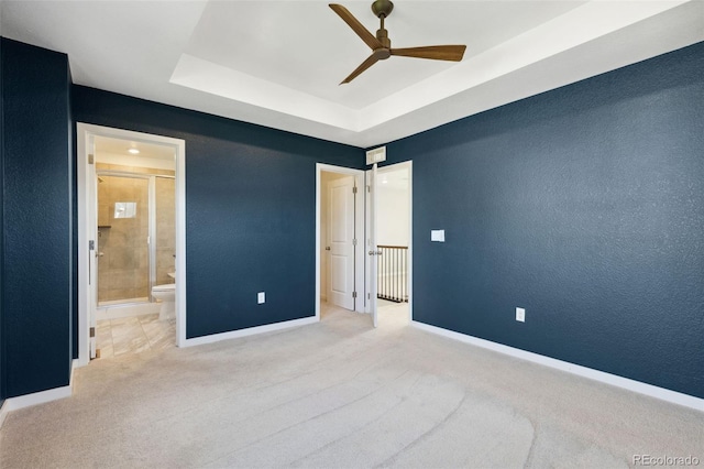 unfurnished bedroom with baseboards, a raised ceiling, carpet flooring, ensuite bath, and a ceiling fan
