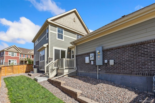 view of property exterior with fence, central AC unit, and brick siding