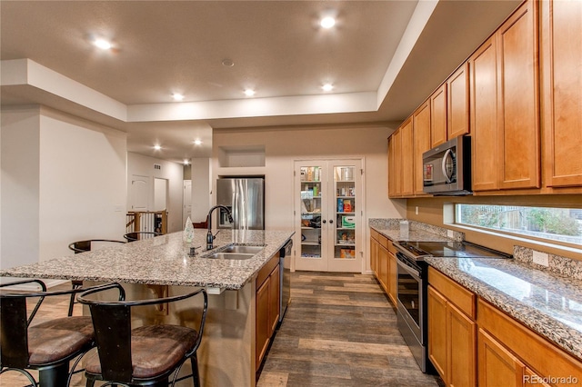 kitchen with dark wood-type flooring, a center island with sink, sink, a breakfast bar, and appliances with stainless steel finishes