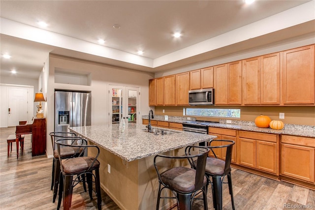 kitchen with hardwood / wood-style floors, a center island with sink, appliances with stainless steel finishes, a breakfast bar, and sink