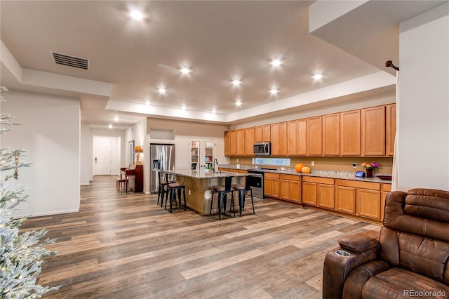 kitchen featuring appliances with stainless steel finishes, hardwood / wood-style flooring, a center island with sink, and a breakfast bar area