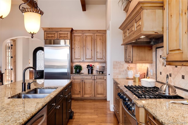 kitchen featuring stainless steel appliances, premium range hood, light stone countertops, and sink