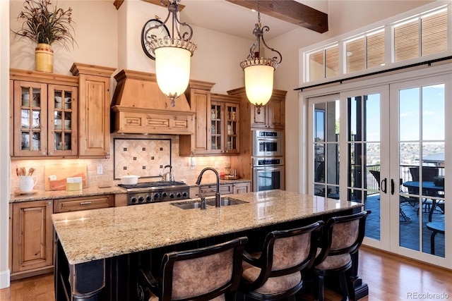 kitchen with tasteful backsplash, an island with sink, sink, a breakfast bar area, and custom exhaust hood