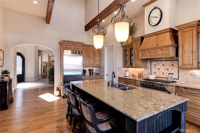 kitchen featuring sink, premium range hood, a kitchen island with sink, premium appliances, and beamed ceiling