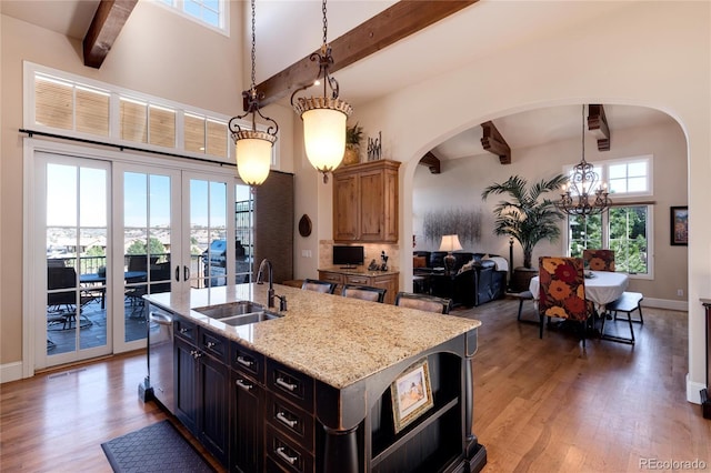 kitchen with sink, dishwasher, a kitchen island with sink, light stone countertops, and decorative light fixtures