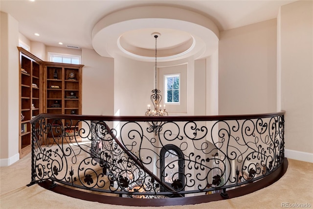 corridor with a notable chandelier, a tray ceiling, and light colored carpet