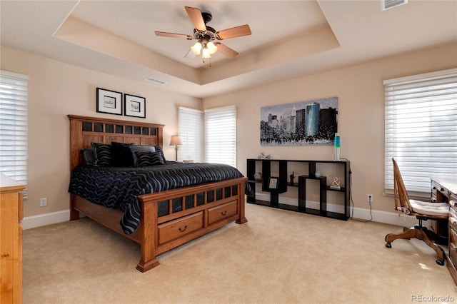 bedroom with ceiling fan, a tray ceiling, and light carpet