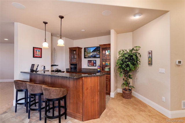 bar with dark stone counters, decorative light fixtures, and light carpet