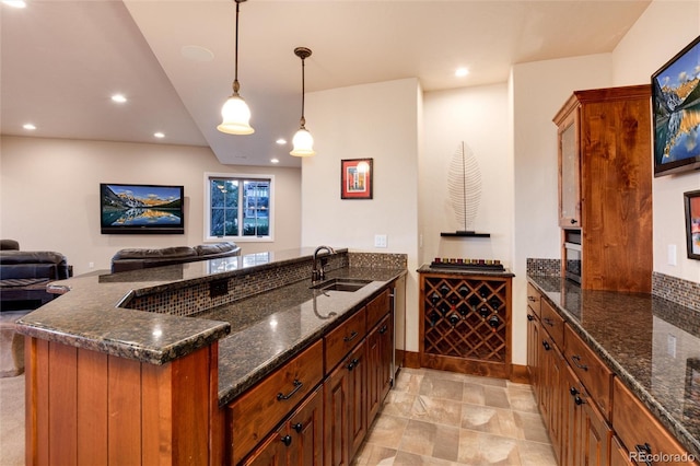 interior space with hanging light fixtures, sink, dark stone countertops, and kitchen peninsula