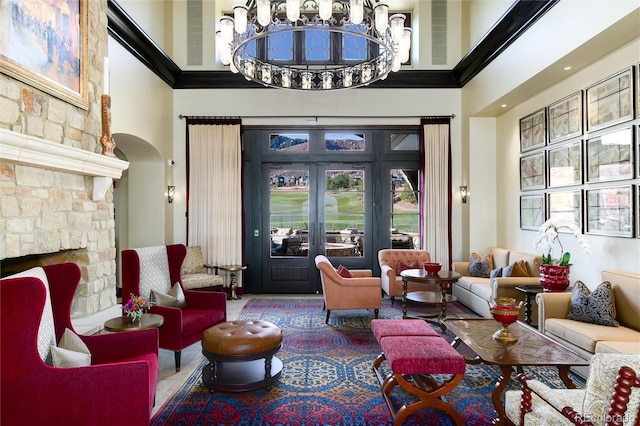 interior space featuring a notable chandelier, a towering ceiling, a stone fireplace, and french doors