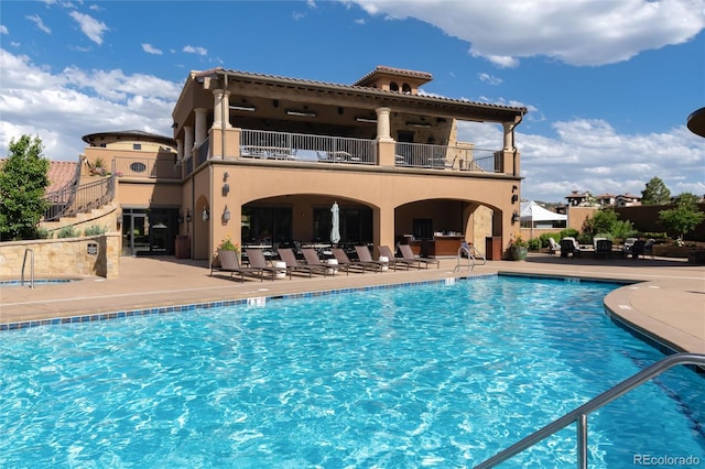 rear view of house featuring a community pool, a patio area, and a balcony