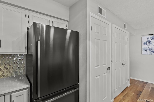 kitchen featuring freestanding refrigerator, backsplash, light wood finished floors, white cabinets, and a textured ceiling