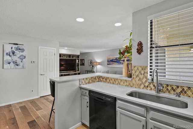 kitchen featuring dishwasher, a sink, light wood-type flooring, backsplash, and light countertops