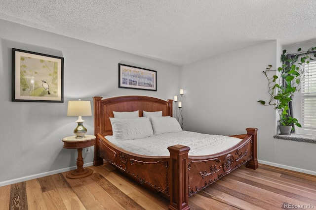 bedroom with wood finished floors, a textured ceiling, and baseboards