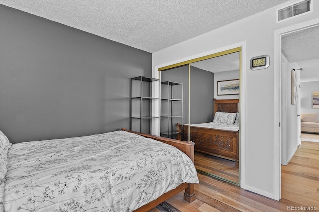 bedroom with a textured ceiling, wood finished floors, a closet, and baseboards