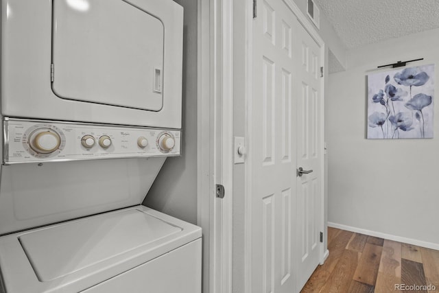 clothes washing area featuring stacked washing machine and dryer, wood finished floors, baseboards, and a textured ceiling