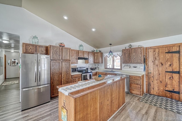 kitchen with decorative light fixtures, a center island, sink, light wood-type flooring, and stainless steel appliances