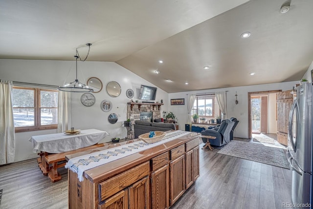 kitchen with hardwood / wood-style floors, stainless steel fridge, a stone fireplace, vaulted ceiling, and pendant lighting