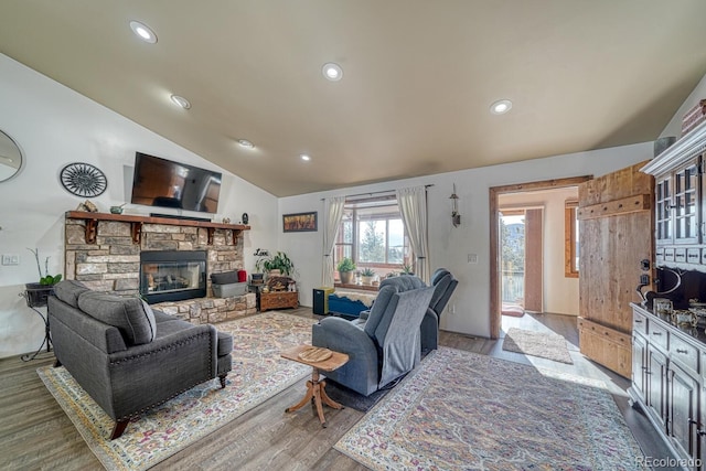 living room featuring light wood-type flooring, a stone fireplace, and vaulted ceiling