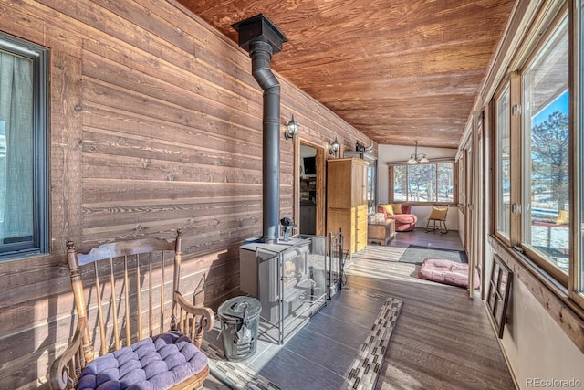 unfurnished sunroom with vaulted ceiling, ceiling fan, wood ceiling, and a wood stove