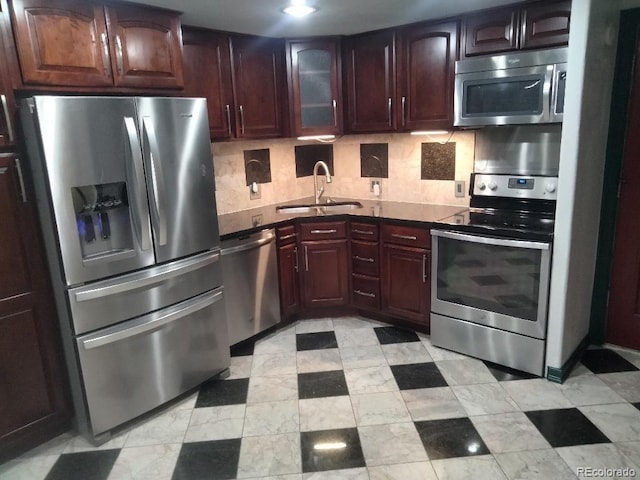 kitchen with a sink, glass insert cabinets, appliances with stainless steel finishes, dark countertops, and tasteful backsplash