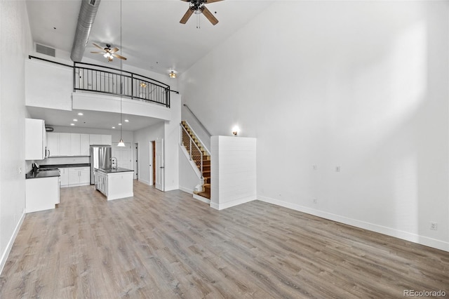 7700 E 29th Ave Unit 102, Denver, CO 80238 - unfurnished living room with a towering ceiling, a ceiling fan, stairs, baseboards, and light wood finished floors