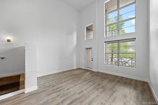 7700 E 29th Ave Unit 102, Denver, CO 80238 - unfurnished living room featuring a towering ceiling, light wood-style flooring, and baseboards