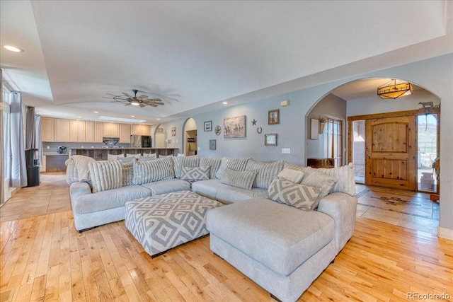 living area featuring arched walkways, light wood-style floors, and ceiling fan