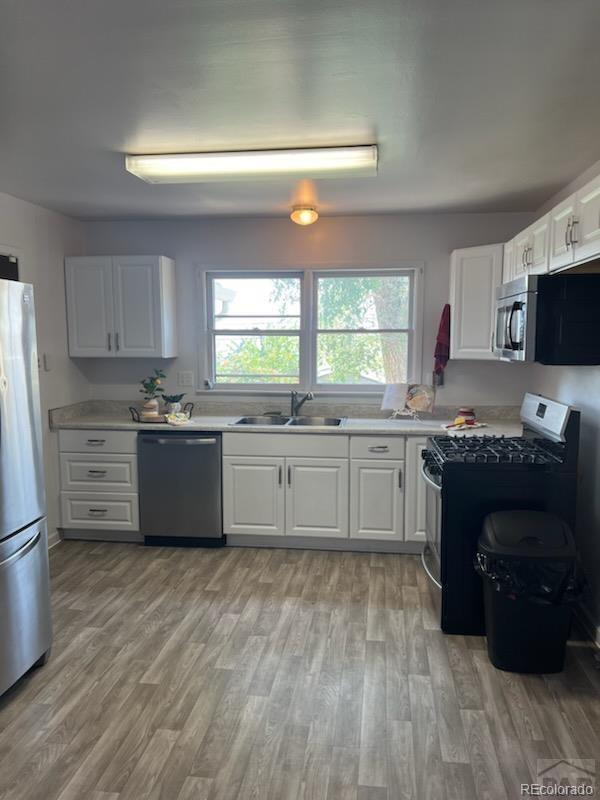 kitchen with appliances with stainless steel finishes, sink, white cabinets, and light hardwood / wood-style floors