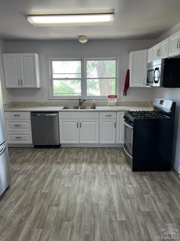 kitchen with white cabinetry, stainless steel appliances, sink, and light hardwood / wood-style floors