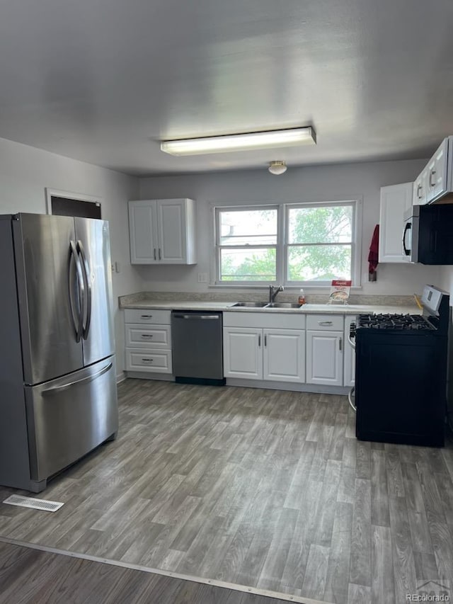 kitchen featuring light wood-type flooring, appliances with stainless steel finishes, white cabinetry, and sink